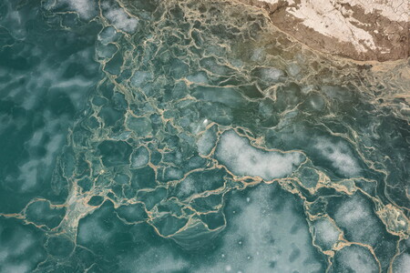 Abstract aerial view of a thawing lake with ice floes and flower pollen forming streaks on the water