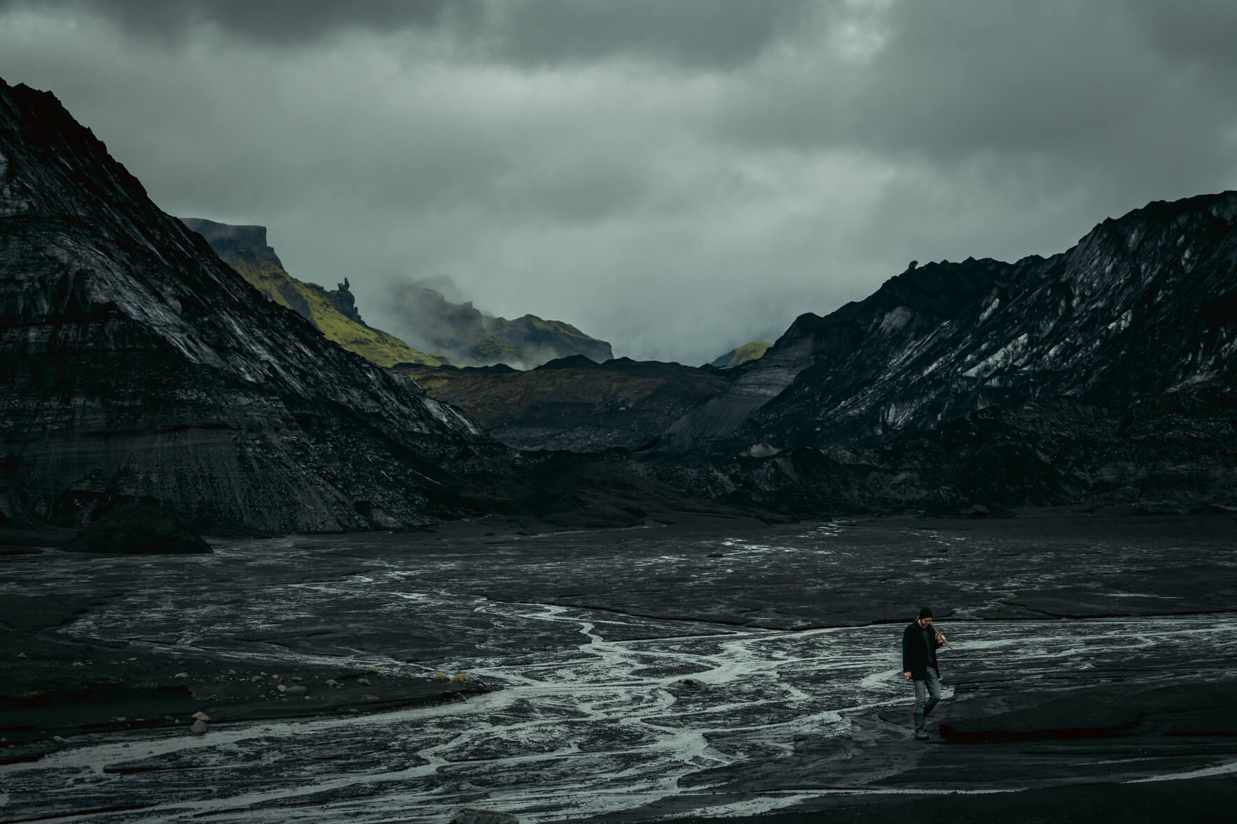 Moody glacier landscape of Iceland with man walking in glacial river bed