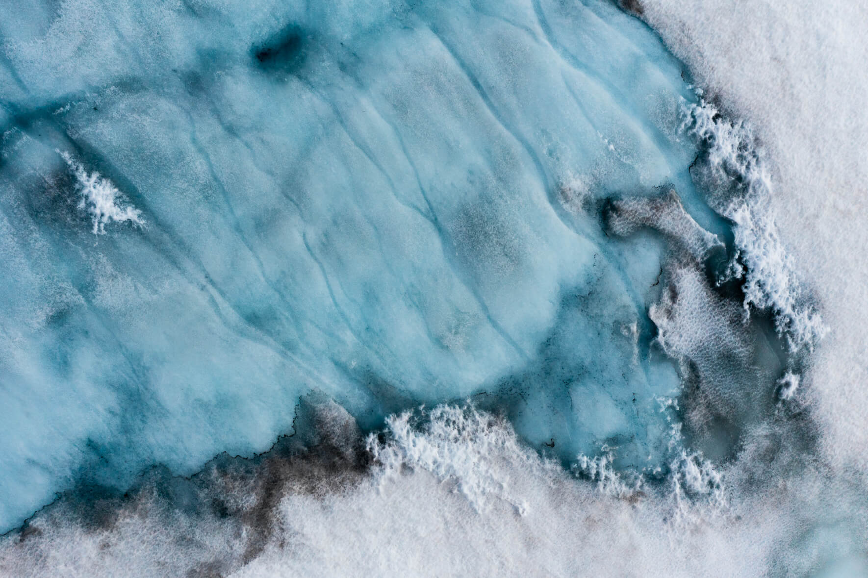 Aerial view of a snow-covered glacier in Norway with meltwater puddles