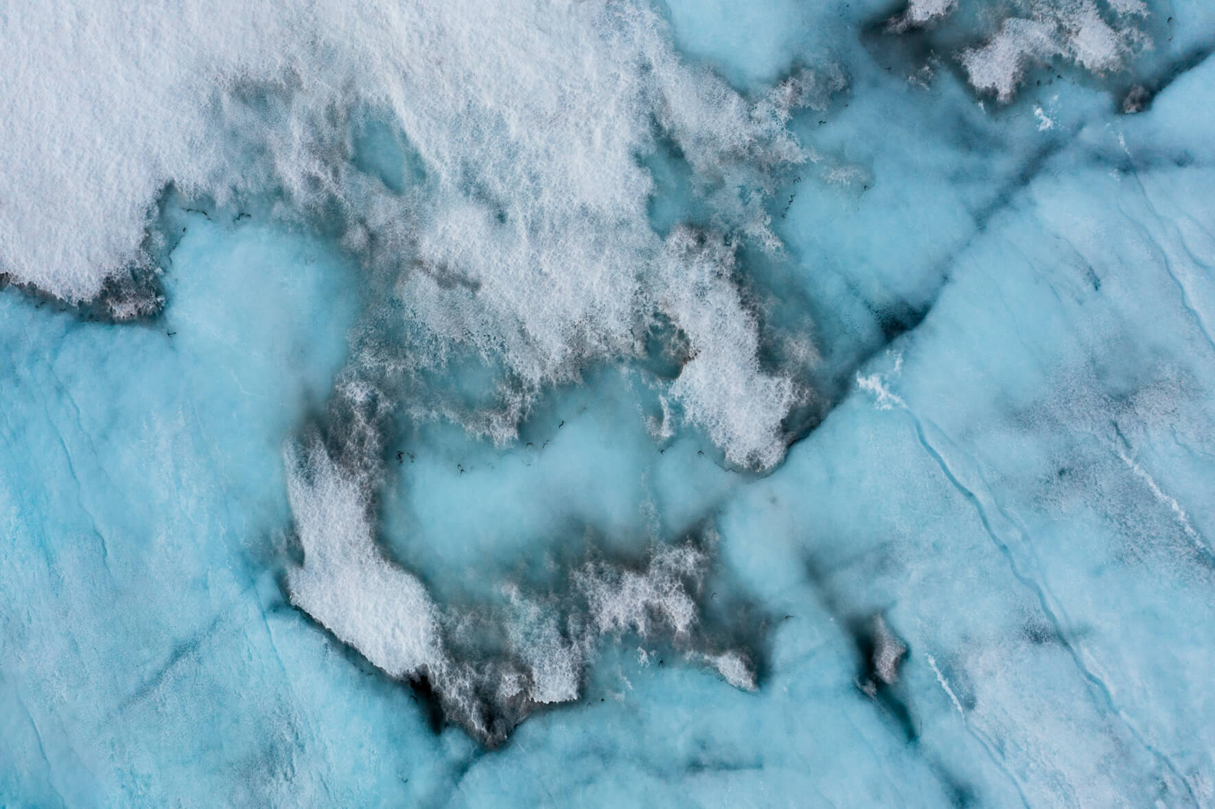 Aerial view of a snow-covered glacier in Norway with meltwater puddles in early summer