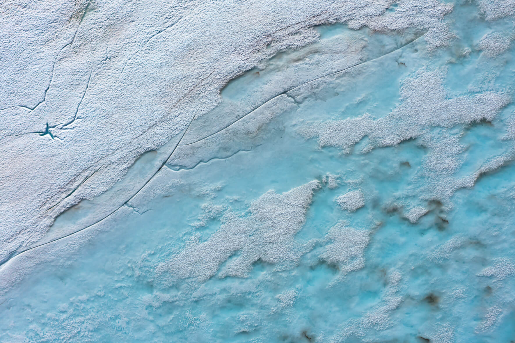 Meltwater lakes on a frozen lake in Southern Norway in early summer with cracks in the ice surface