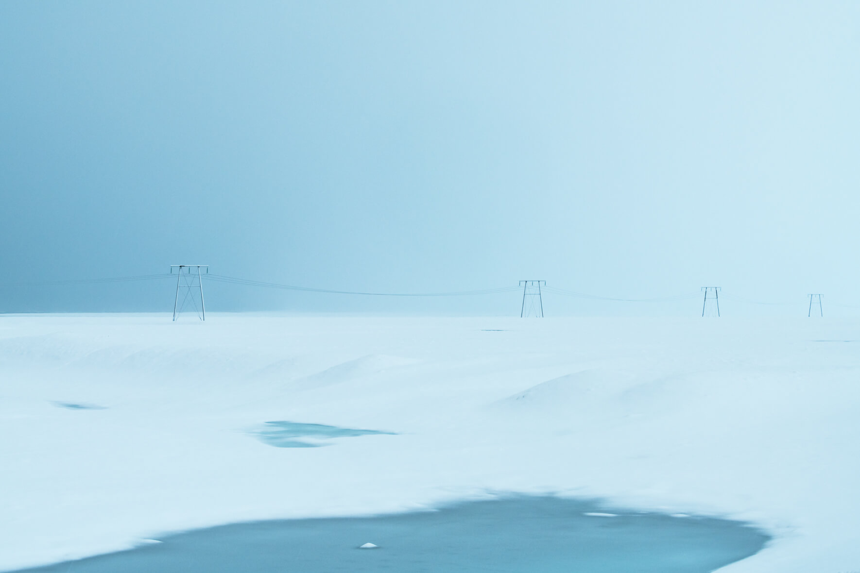 A row of power poles in minimalist winter landscape with lake in the foreground