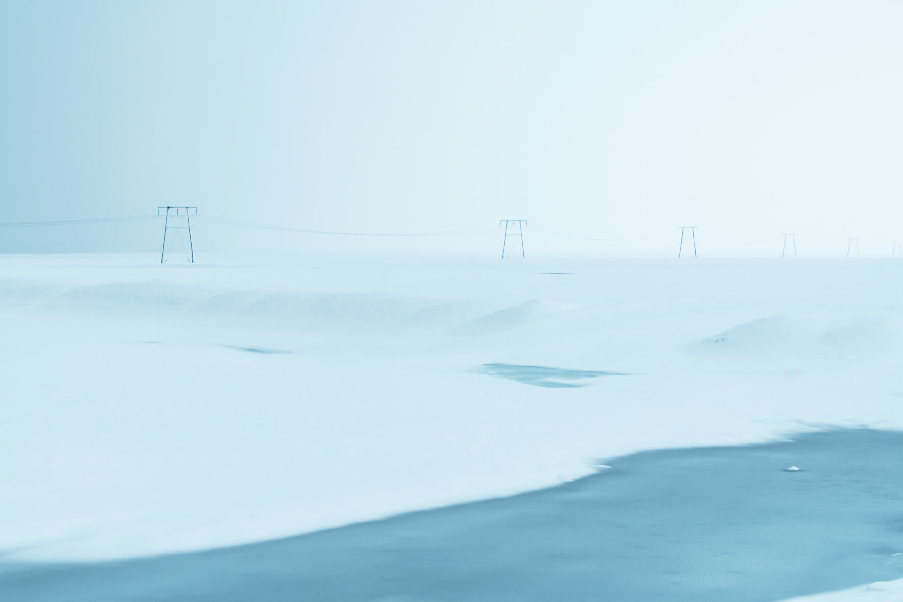 A row of power poles in minimalist winter landscape with frozen river