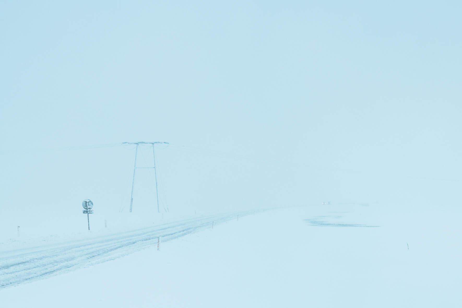 Snowy road during a dangerous winter storm in Iceland with power poles in the background