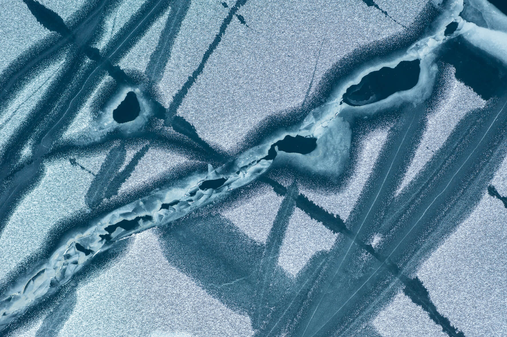 Cracks and open channels in the ice of a frozen lake caused by fluctuations in temperature