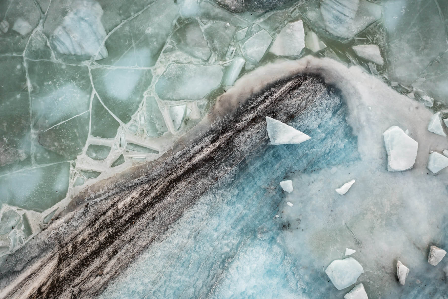 Drone perspective of Svínafellslón in winter, where ice formations reflect blues, greens, and earthy tones