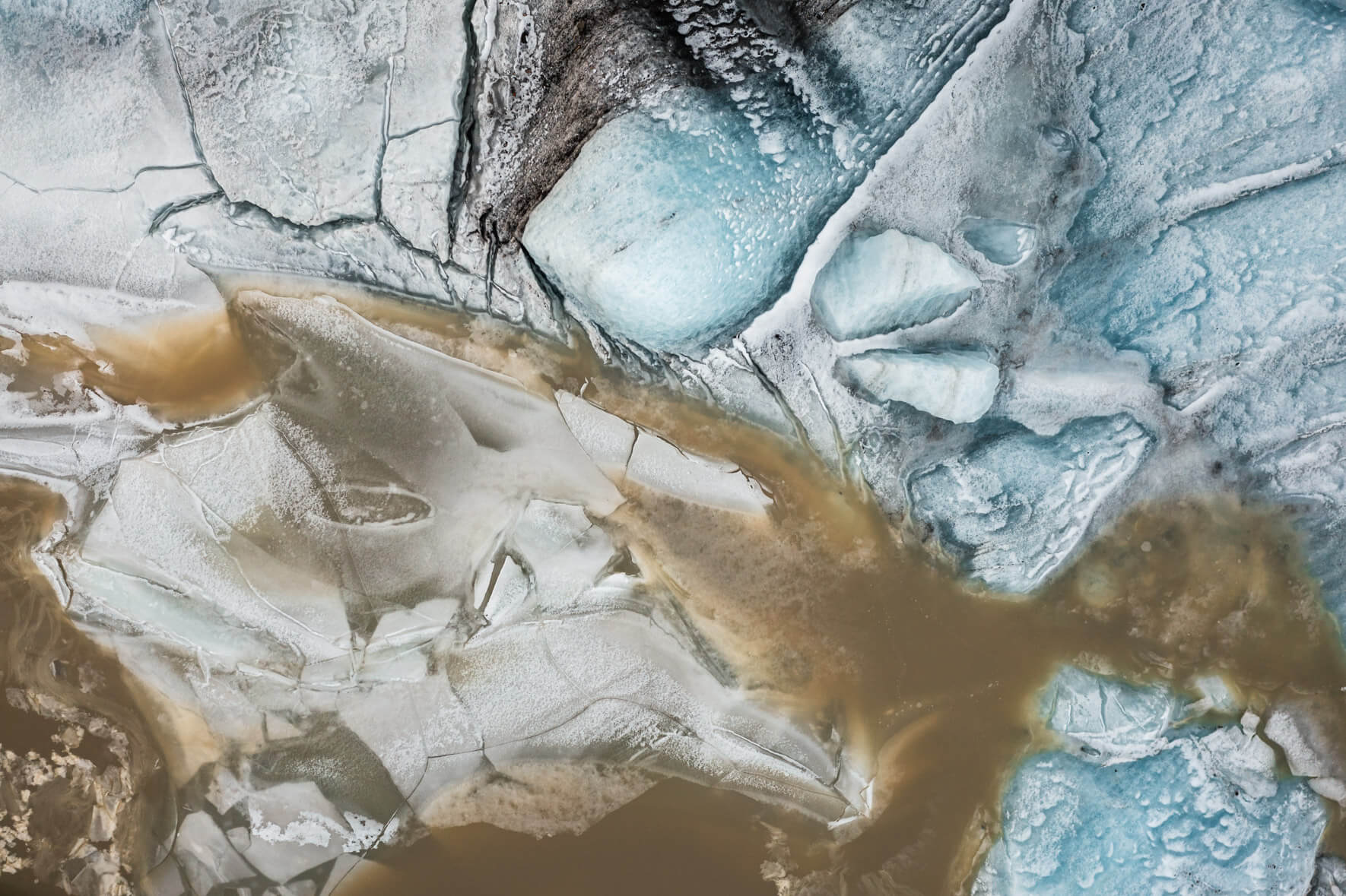 Drone perspective of Svínafellslón in winter, where ice formations reflect blues, greens, and earthy tones