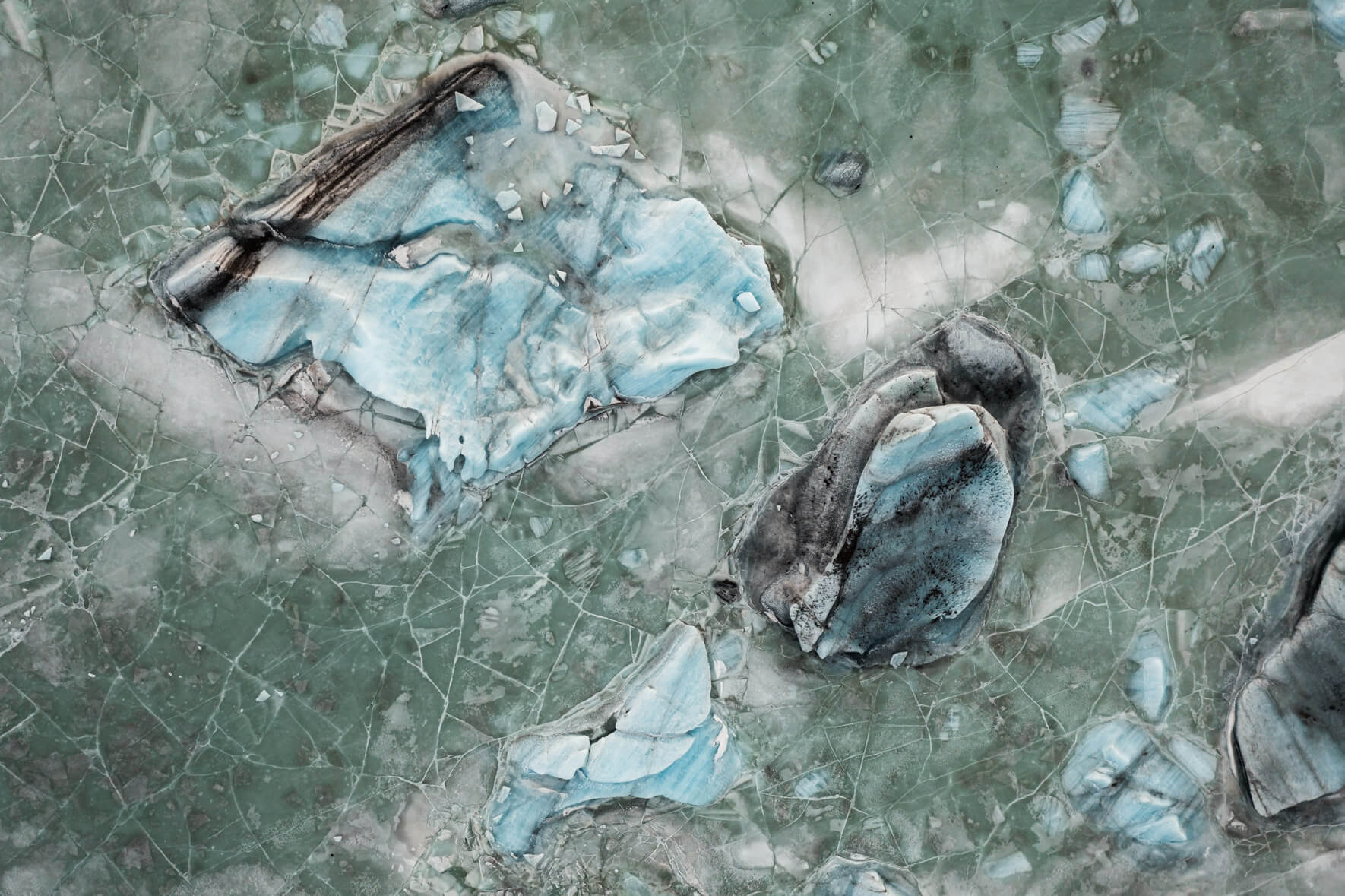 Aerial perspective of Svínafellslón glacial lagoon, where ice, minerals, and air bubbles form striking hues