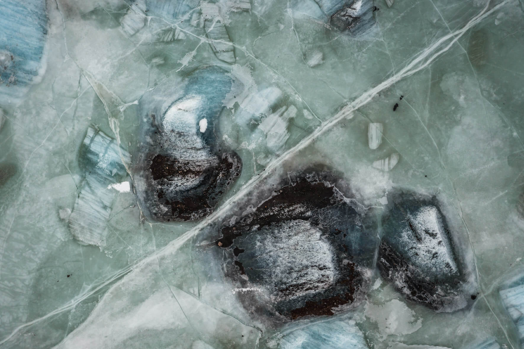 Aerial perspective of Svínafellslón glacial lagoon, where ice, minerals, and air bubbles form striking hues