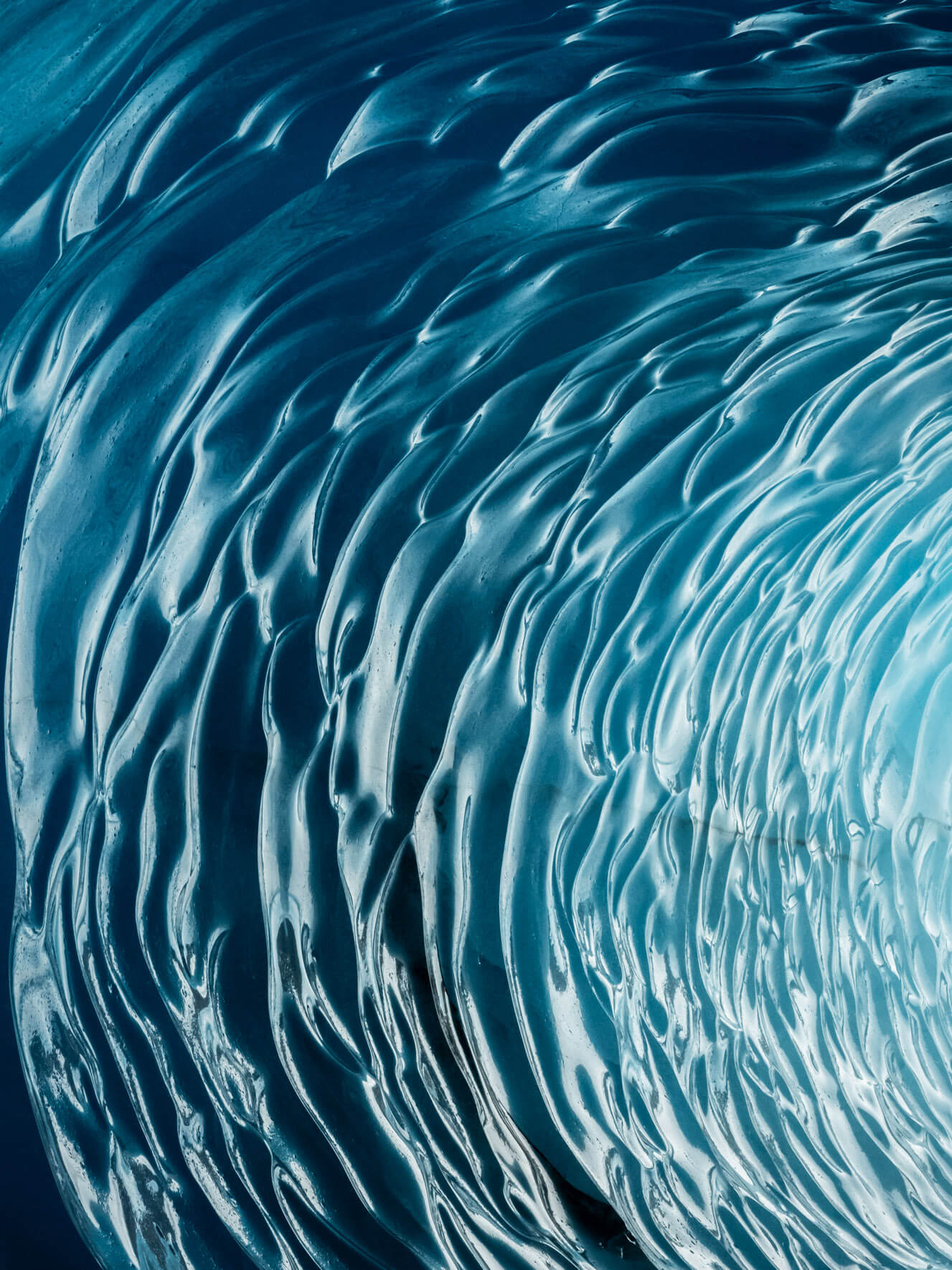 Inside of a frozen iceberg tunnel, showing polished surfaces and intense blue tones