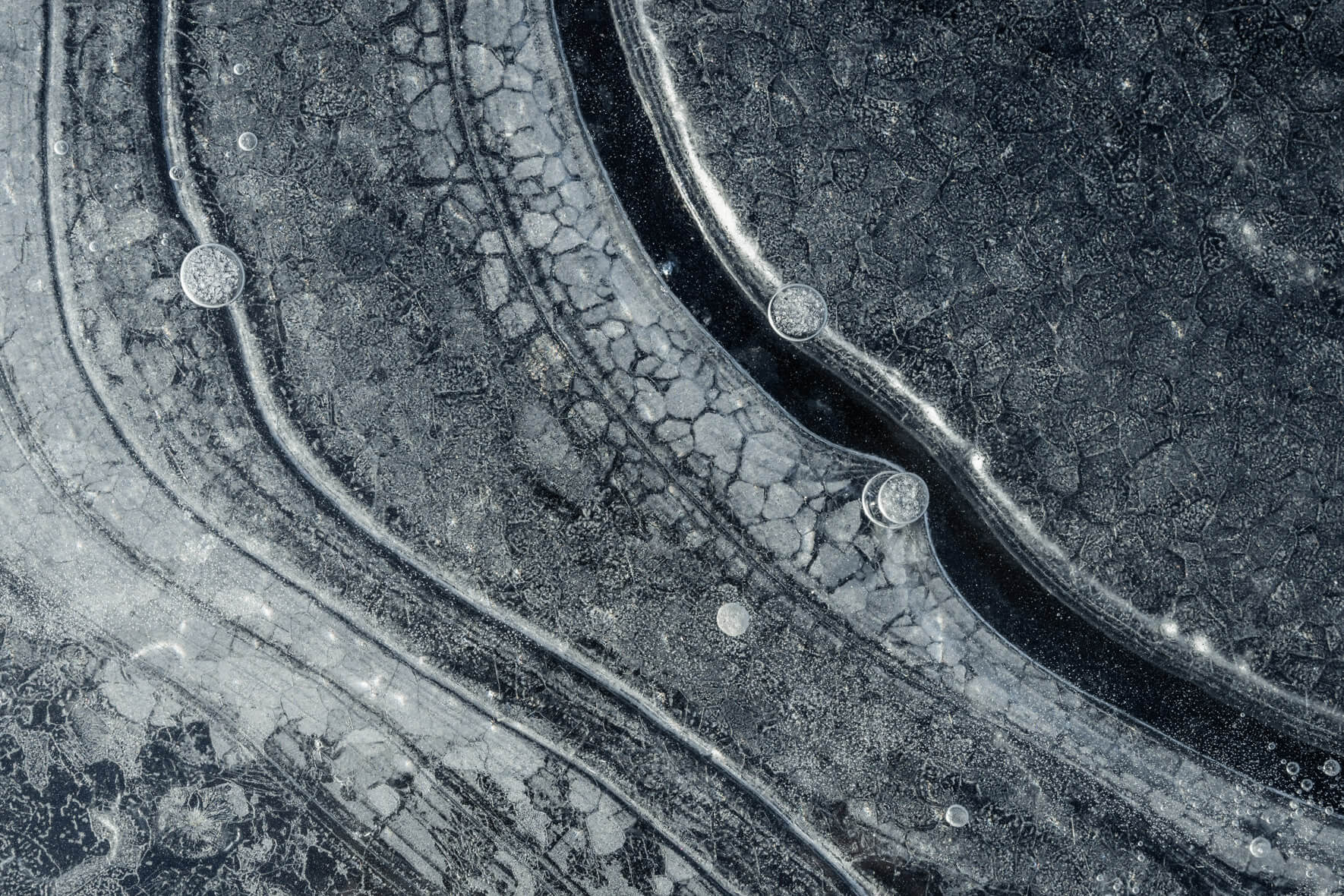 Macro photography of air bubbles trapped in dark ice with intricate patterns