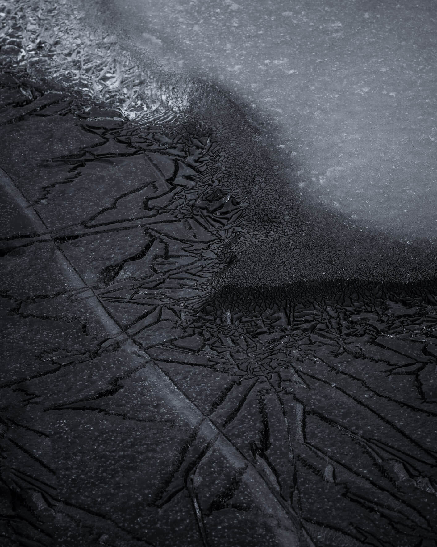 Detailed close-up of Iceland’s frozen lake shore, focusing on dark ice formations and subtle surface cracks