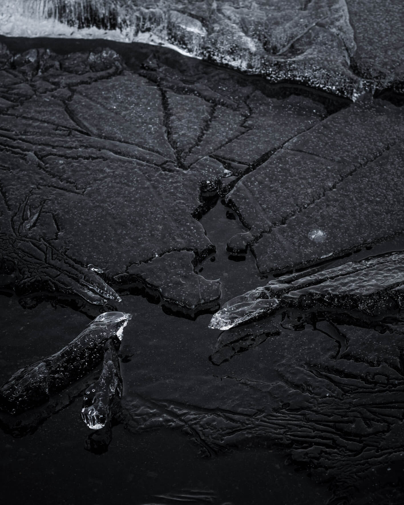 Detailed close-up of Iceland’s frozen lake shore, focusing on dark ice formations and subtle surface cracks