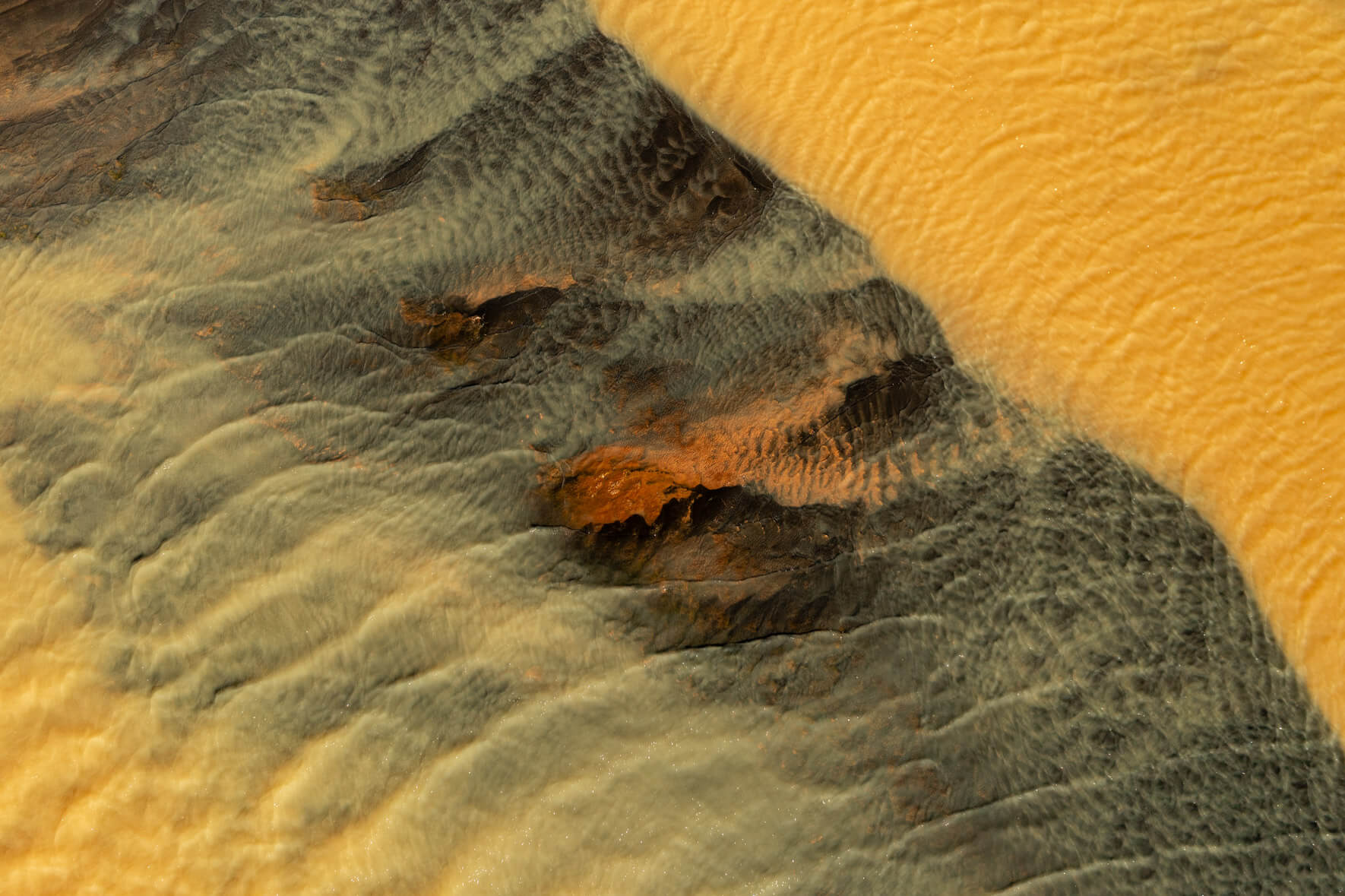 Aerial view of a sulphur-rich river in Iceland, displaying vibrant yellow hues due to geothermal activity