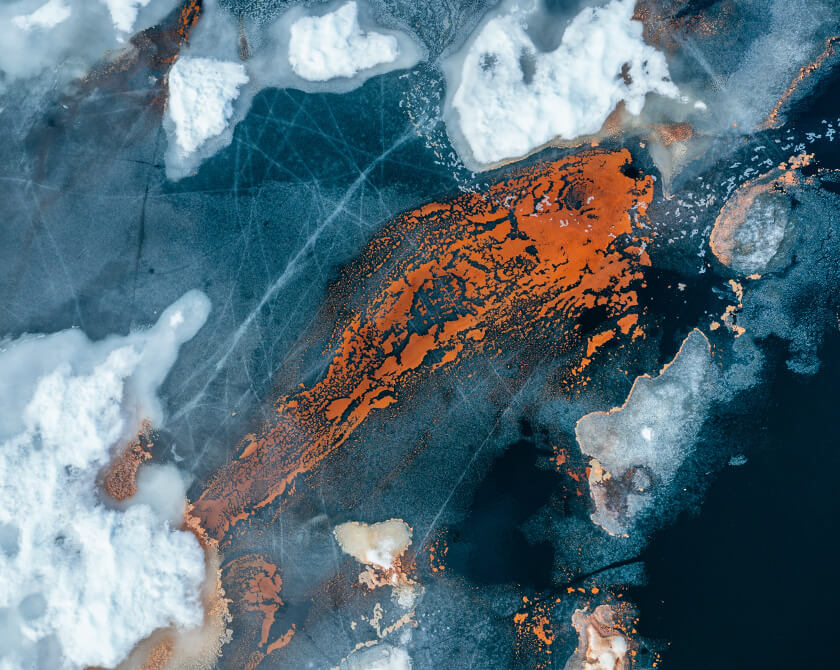 Aerial view of a thawing lake in Norway with ice floes and red pollen in the shape of a fish