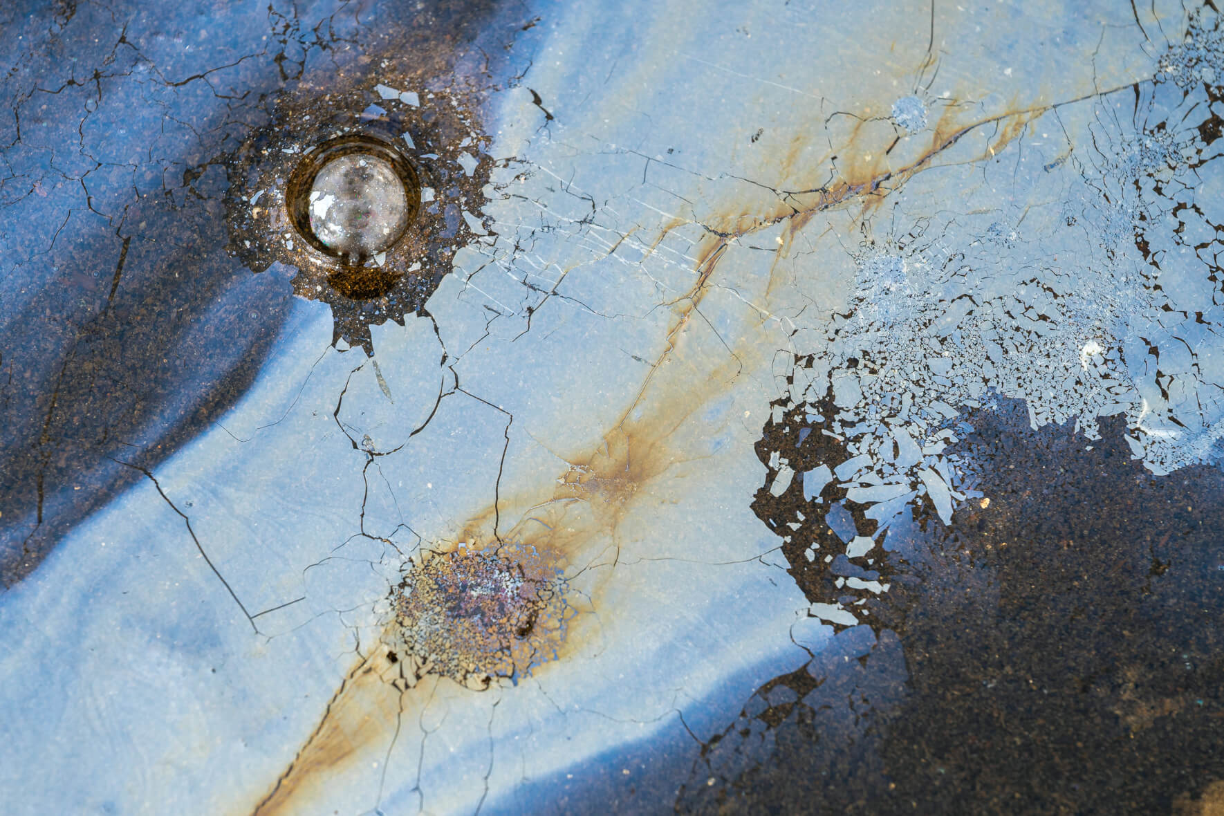 Abstract pattern of iron oxide biofilm with metallic sheen and fractured texture