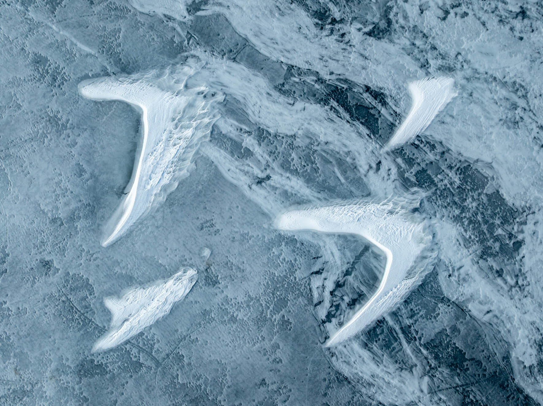 Aerial view of cracked frozen lake with white snow drifts shaped like bird wings