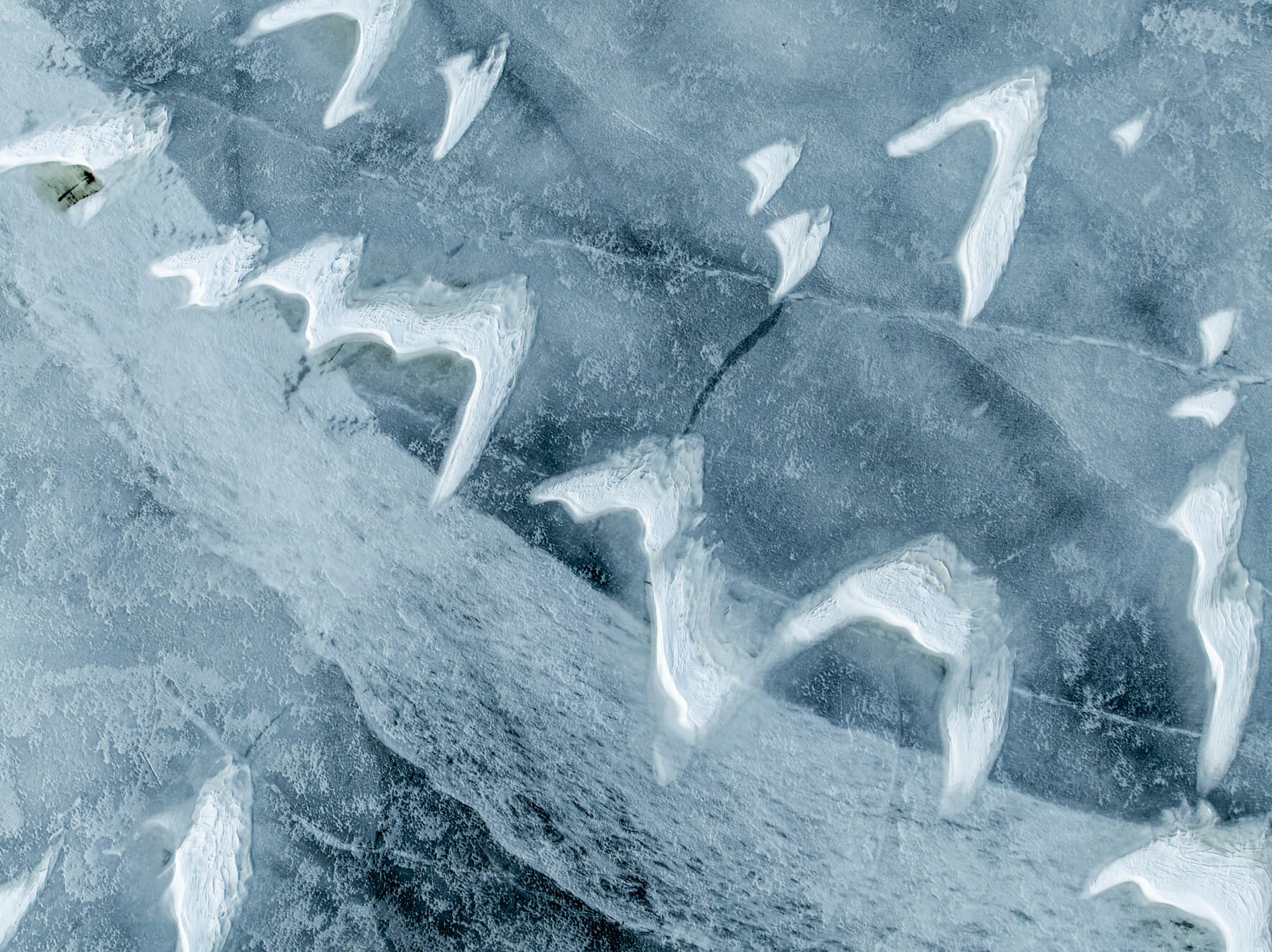 Aerial view of cracked frozen lake in Norway with snow drifts shaped like bird wings