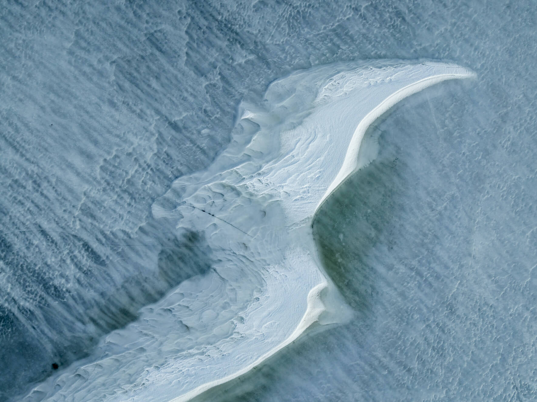 Aerial view of fractured ice with snow-covered ridges and subtle turquoise tones