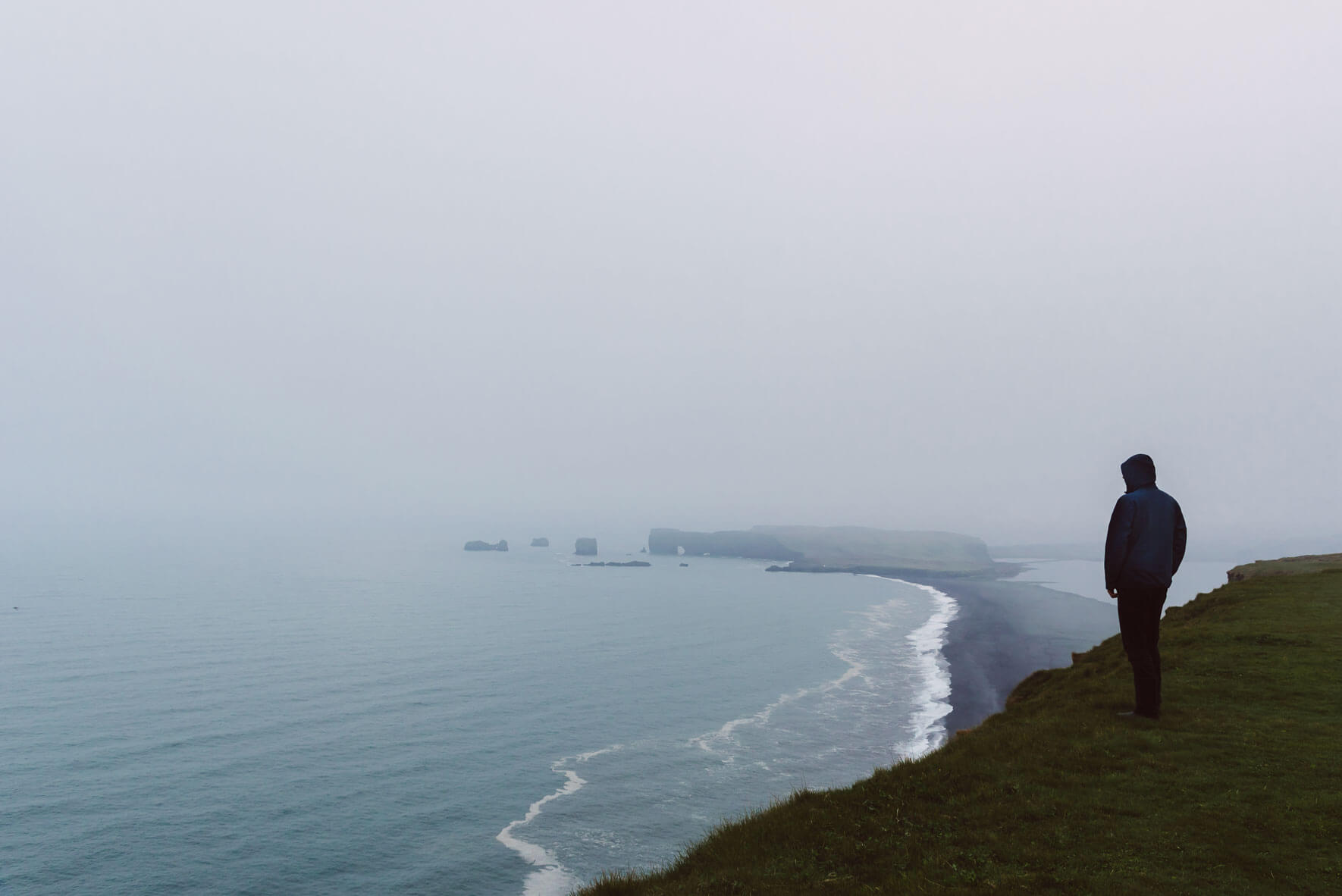 Man standing on Reynisfjall mountain and watching over Dyrhólaey, Iceland